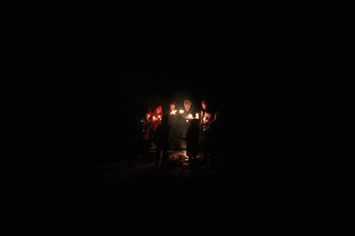 A group of people holding hands in prayer around a glowing candle.