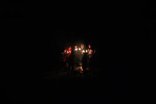 A circle of people holding hands in a cozy room lit by soft candles, creating a warm and inviting atmosphere.