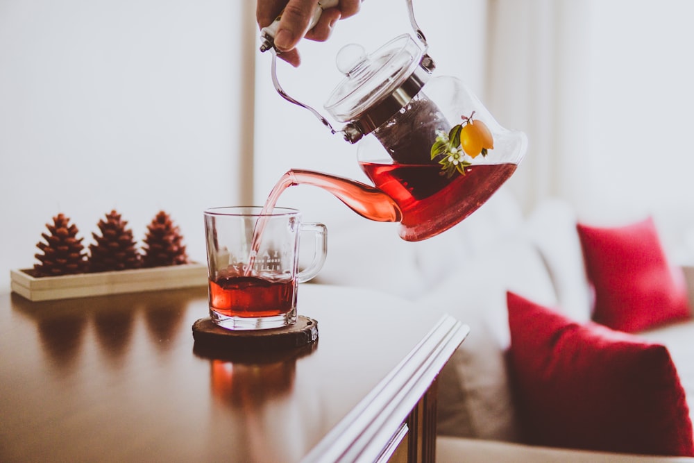 person holding teapot pouring up on glass mug