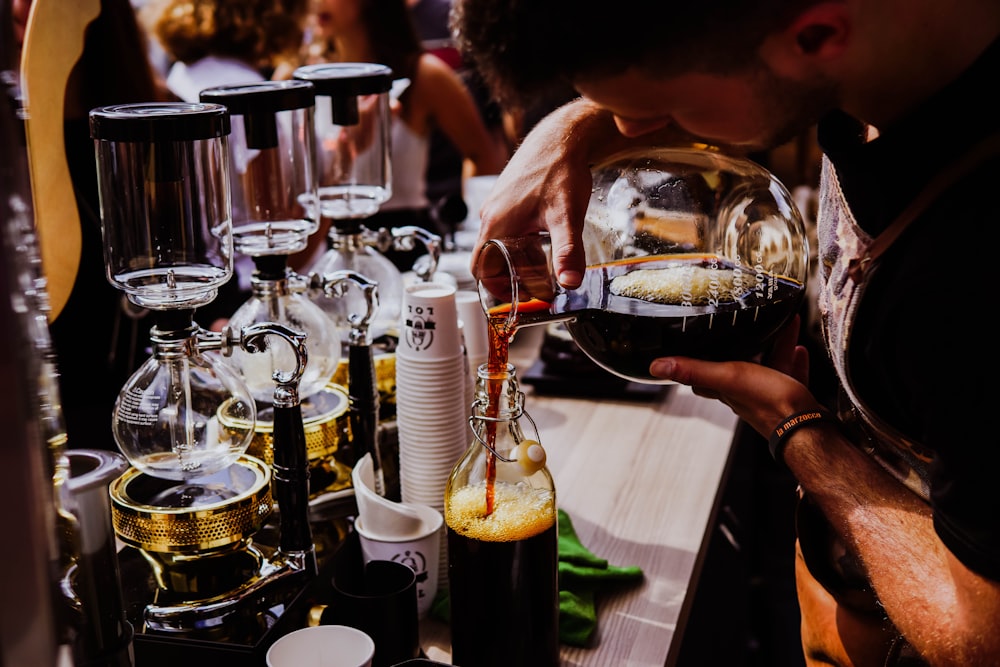 person holding clear glass bottle pouring black liquid on clear glass bottle