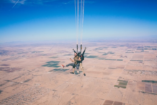 two men in 1 parachute in mid air during daytime