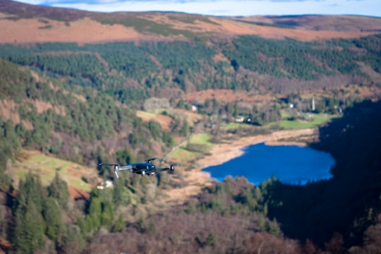 high-angle tilt-shift lens photography of black quadcopter drone hovering above forested valley during daytime in Glendalough Ireland