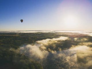 A hot air balloon soaring gently over a lush green landscape at sunrise.