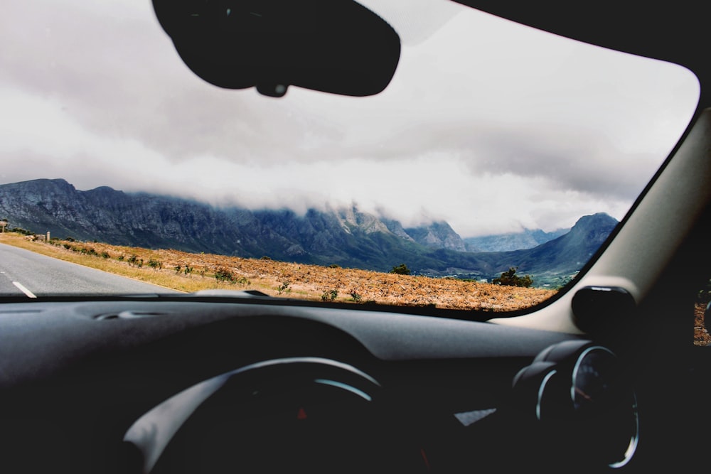 photo of car on road beside brown open field during cloudy daytime