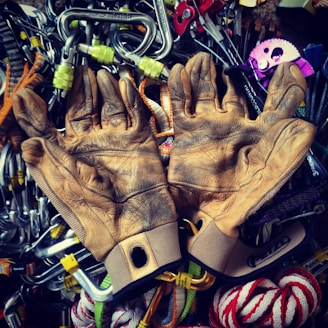Worn leather gloves rest on a pile of climbing gear including carabiners, ropes, and slings. The equipment suggests readiness for a climbing adventure.