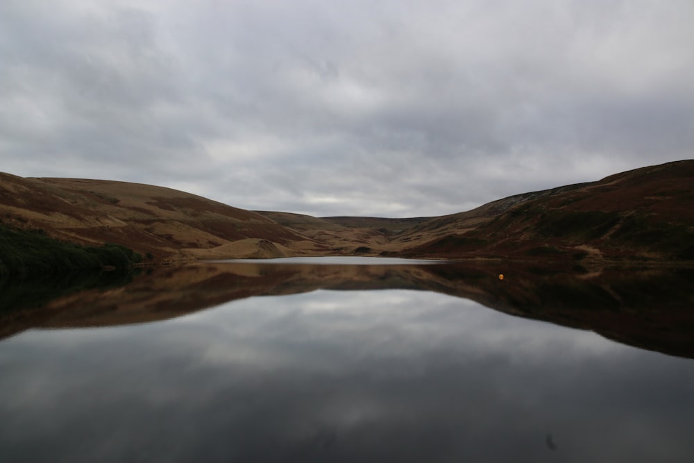 brown mountain beside body of water under white clouds