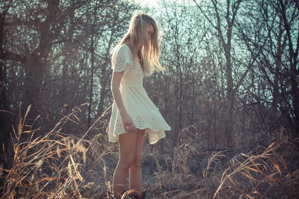 femme portant une robe debout sur un champ de plantes près d’arbres nus