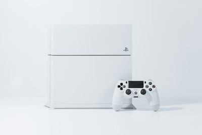 A white gaming console standing upright with a matching white controller placed in front of it. The background is a light, neutral color, accentuating the sleek and modern design of the console.
