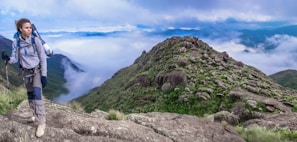 A scenic mountain trail with a hiker pausing to admire the view, budget gear visible.