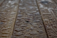 Drops of water scattered across a wooden surface, highlighting the wood grain texture. The surface appears wet with varying sizes of water droplets.