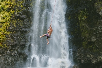man hanging on rope near waterfalls during daytime