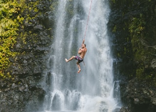 man hanging on rope near waterfalls during daytime