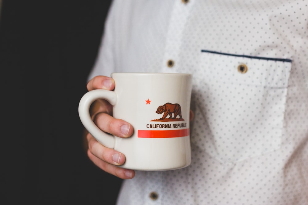 person holding white and red California Republic ceramic mug