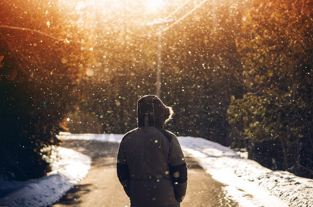 pessoa usando capuz em pé no meio da estrada com neve caindo