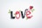 The word 'love' is spelled out using black and red gummy candies shaped like berries, with green candy leaves interspersed. A small white heart-shaped dish filled with additional gummy candies is placed near the word.