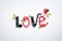 The word 'love' is spelled out using black and red gummy candies shaped like berries, with green candy leaves interspersed. A small white heart-shaped dish filled with additional gummy candies is placed near the word.