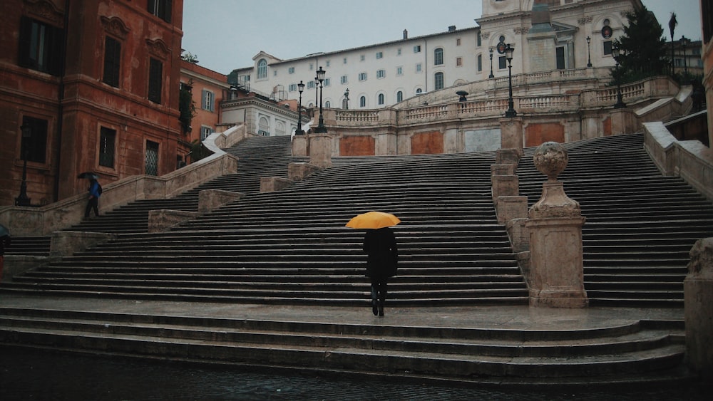 person holding yellow umbrella standing on concrete stairs