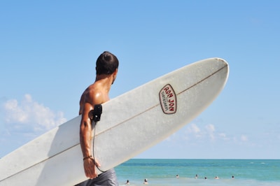 topless man carrying white surfboard in beach during daytime