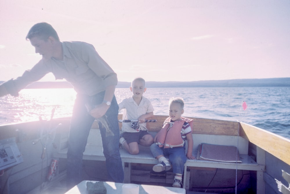 hombre sosteniendo peces grises de pie junto a dos niños sentados en asientos de barco