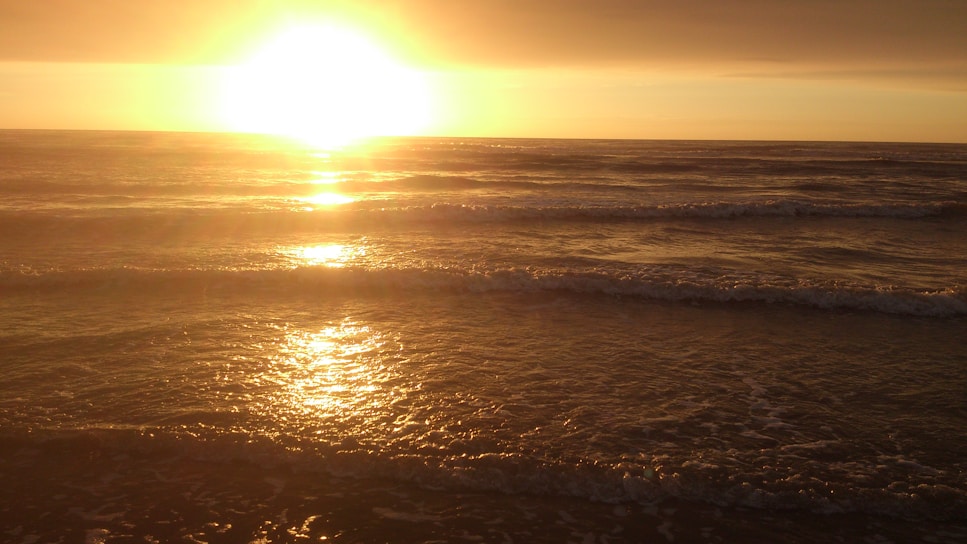 Sunset casting golden hues over a quiet Outer Banks beach with gentle waves.