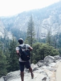 Close-up of a man adjusting his hiking backpack strap amidst tall pine trees.