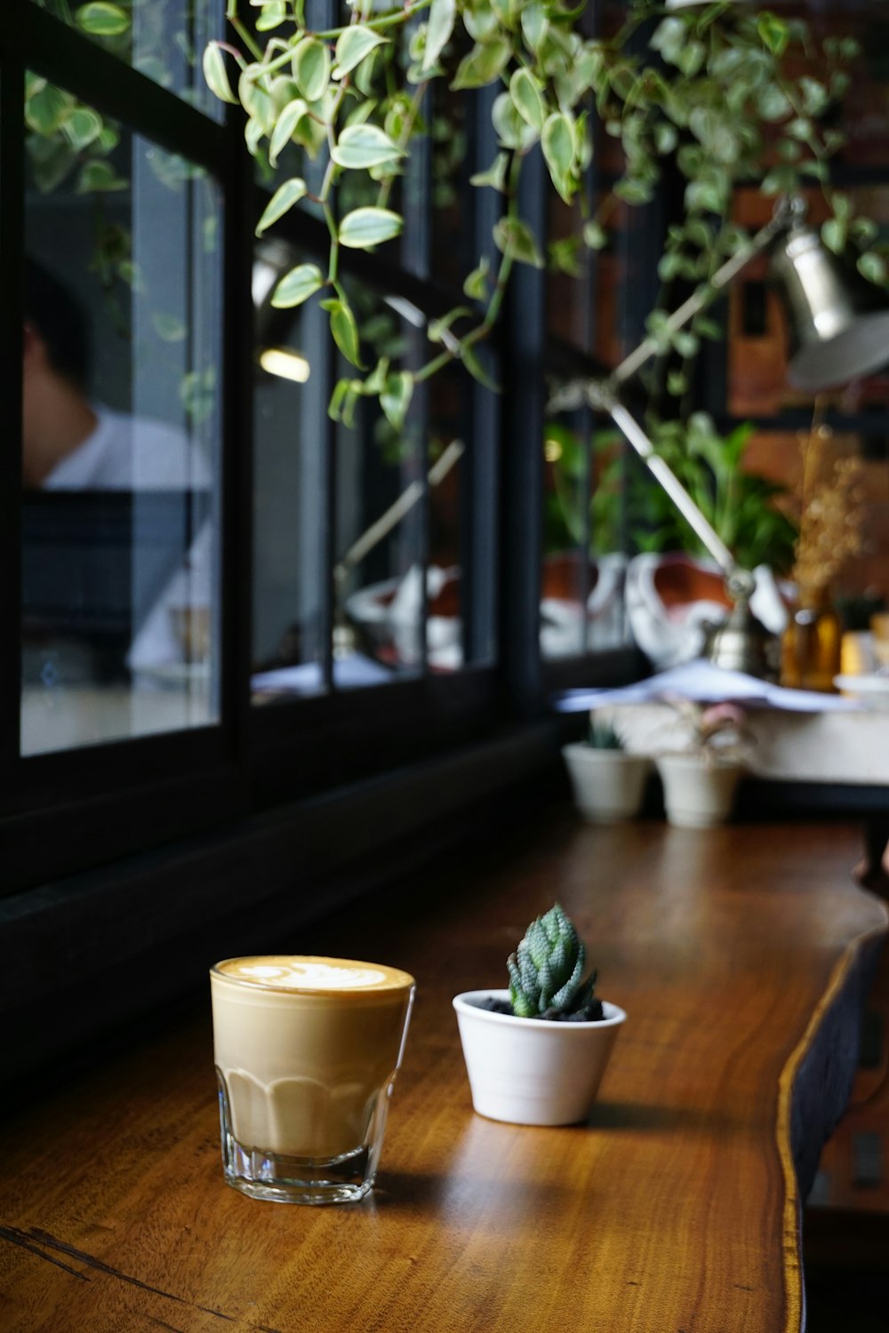 茶色の木製のテーブルにカフェラテとサボテン