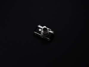 A vintage camera with metallic and black elements is centered on a minimalist, dark background. The camera's intricate details, such as the lens and dials, are highlighted by the low lighting, creating a sense of nostalgia and elegance.