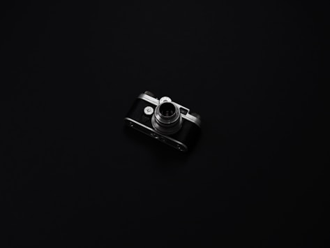 A minimalist black and white photo of a vintage camera on a grey background.
