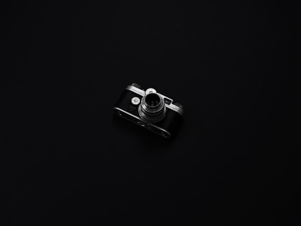 A minimalist still life photograph featuring a vintage camera on a dark surface, with subtle highlights and rich blacks.