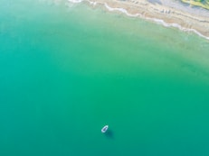 aerial photography of white boat on green ocean near seashore