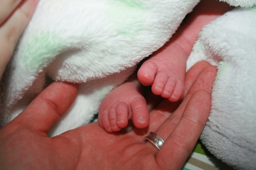 A parent's hands cradling a tiny baby foot wrapped in a cozy pebbloo sleeve.
