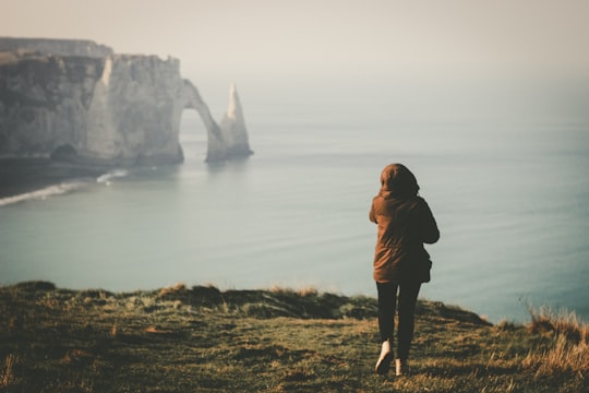 woman walking towards the edge of island facing the ocean during day in Étretat France