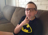 A young African American boy with glasses and a colorful cape.