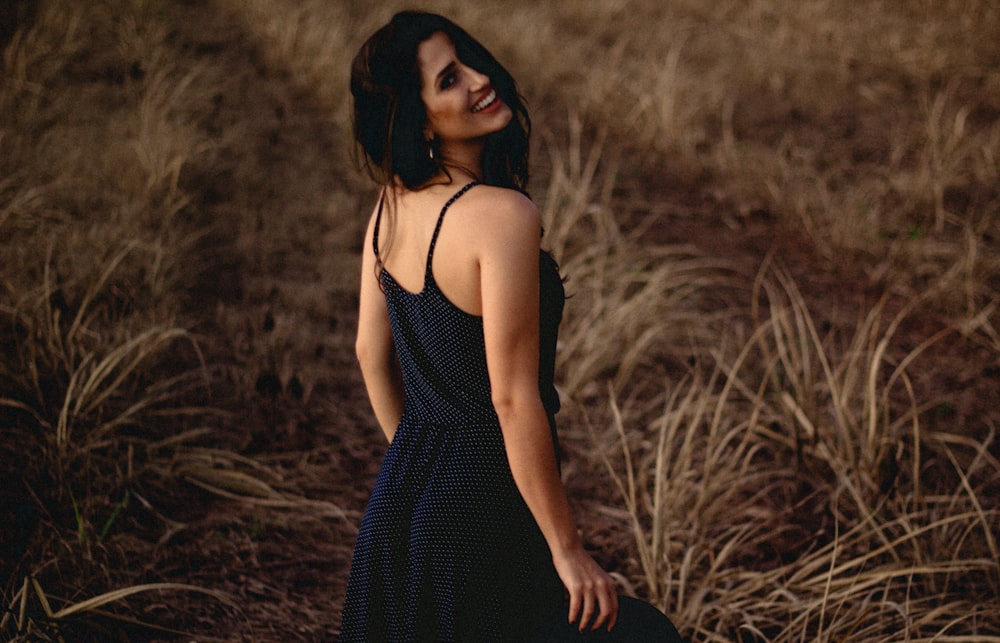 Photographie sélective de mise au point d’une femme en robe noire debout sur un terrain d’herbe