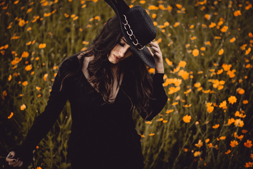 mujer sosteniendo un sombrero que rodea flores de pétalos amarillos