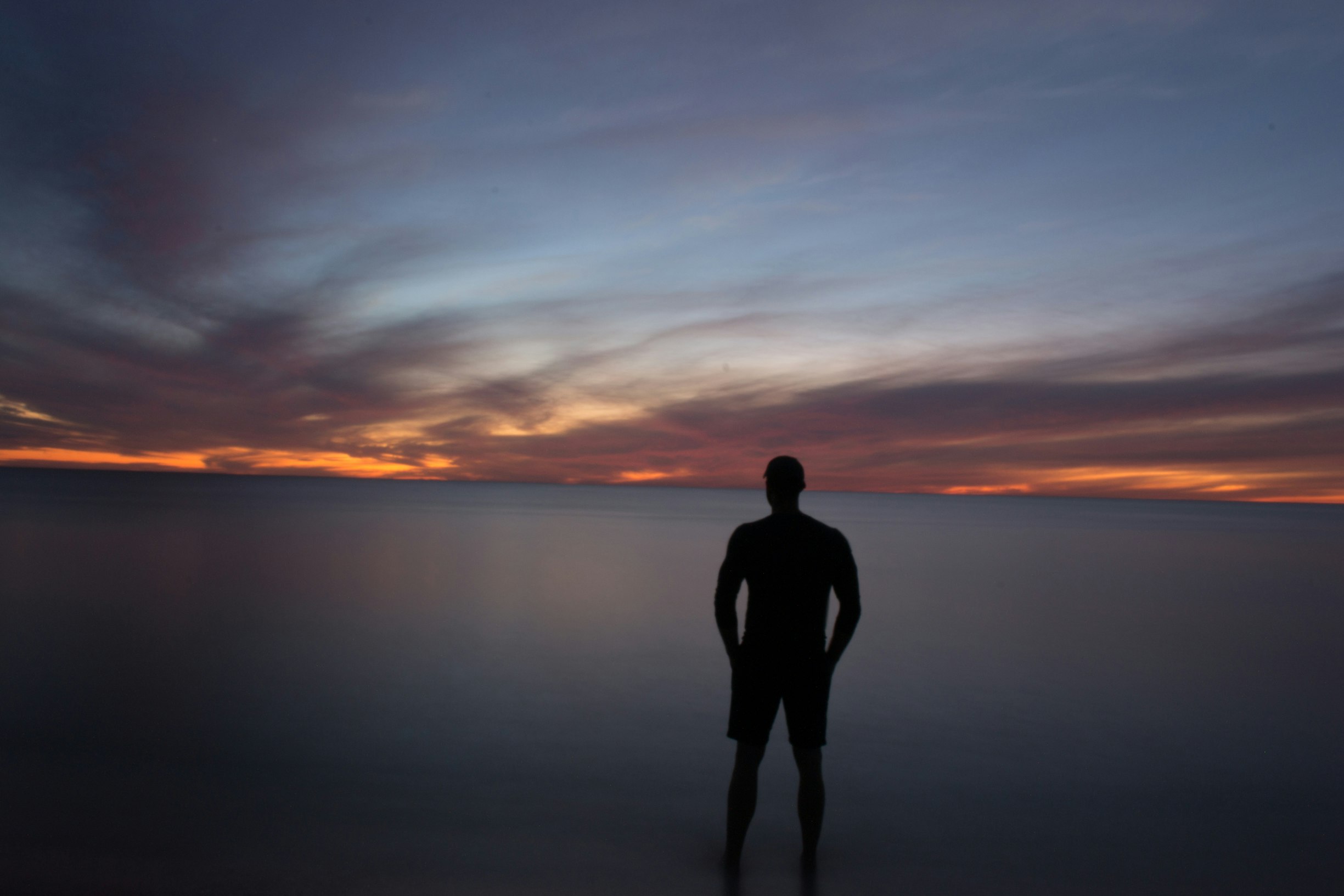 silhouette of person standing near calm body of water during golden hour