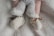 A baby's legs are shown wearing soft, fluffy pants and knitted cream booties with brown ribbon ties, all set against a plush white blanket.