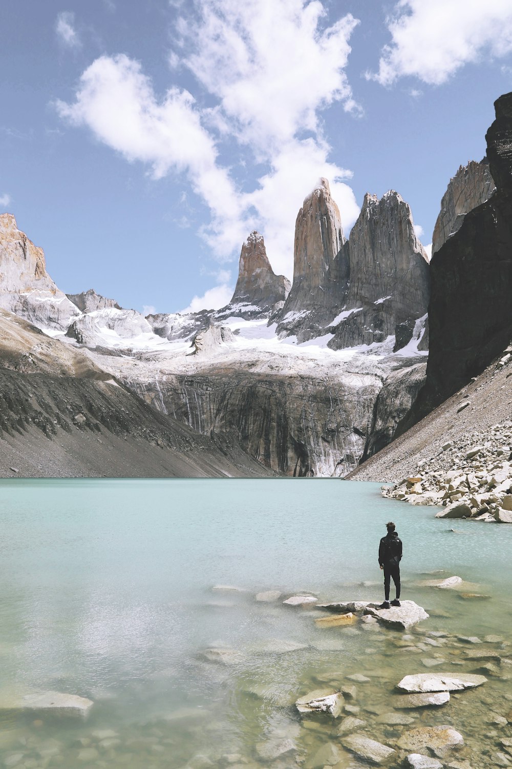 man standing above rock beside body of water under cloudy skies