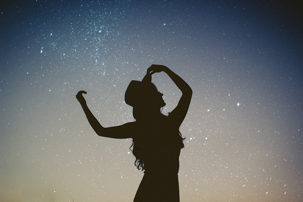 silhouette of woman holding hat in blue and gray nebula