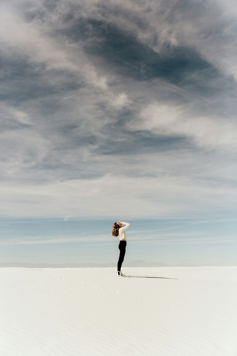 白い砂の上に立って空を見上げる女性