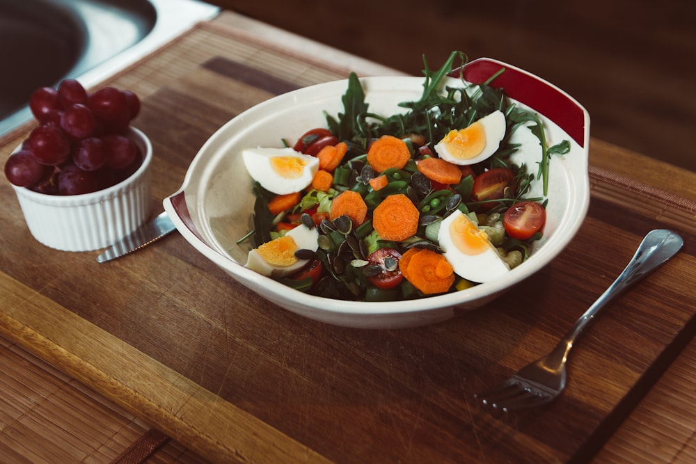 bowl of salad with slide of cooked egg with grapes on the side