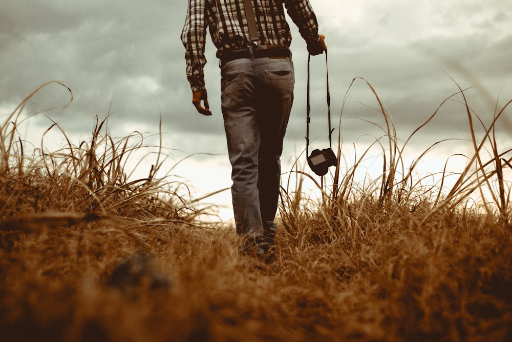 man holding DSLR camera walking through brown grass