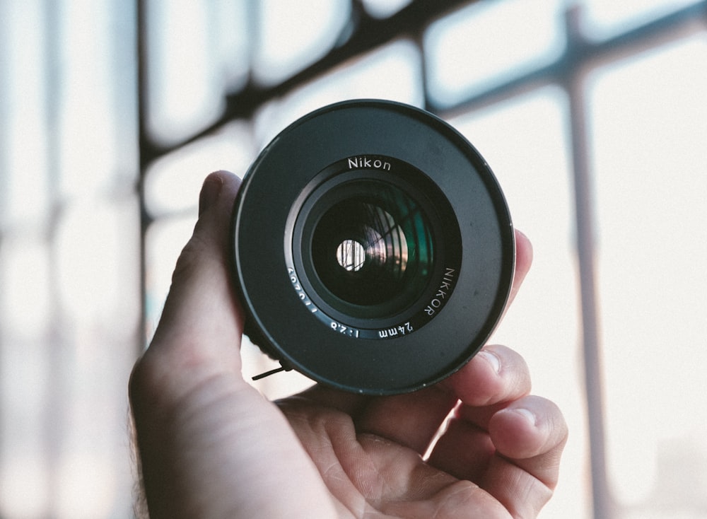 person holding black Nikon camera lens