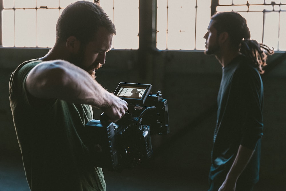 man holding camcorder with man near wall