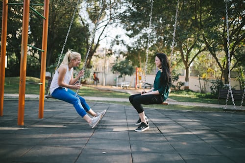Instagram photo of two young women sitting on swings and laughing. 