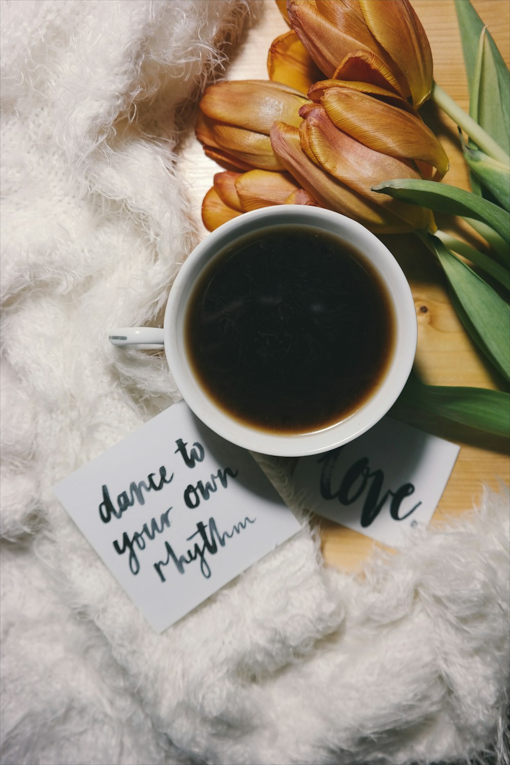 A black cup of coffee in a small cup, surrounded by flowers.