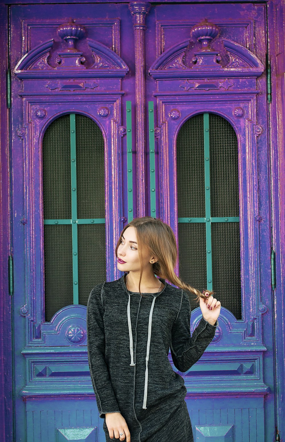 A woman holding her long hair while standing in front of a blue and purple building.