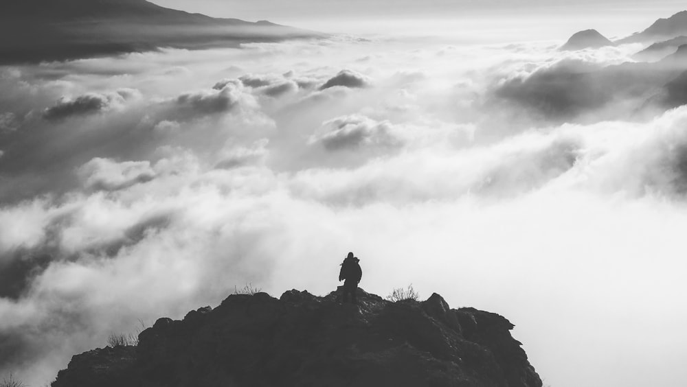 person standing at the edge of a mountain facing clouds during day