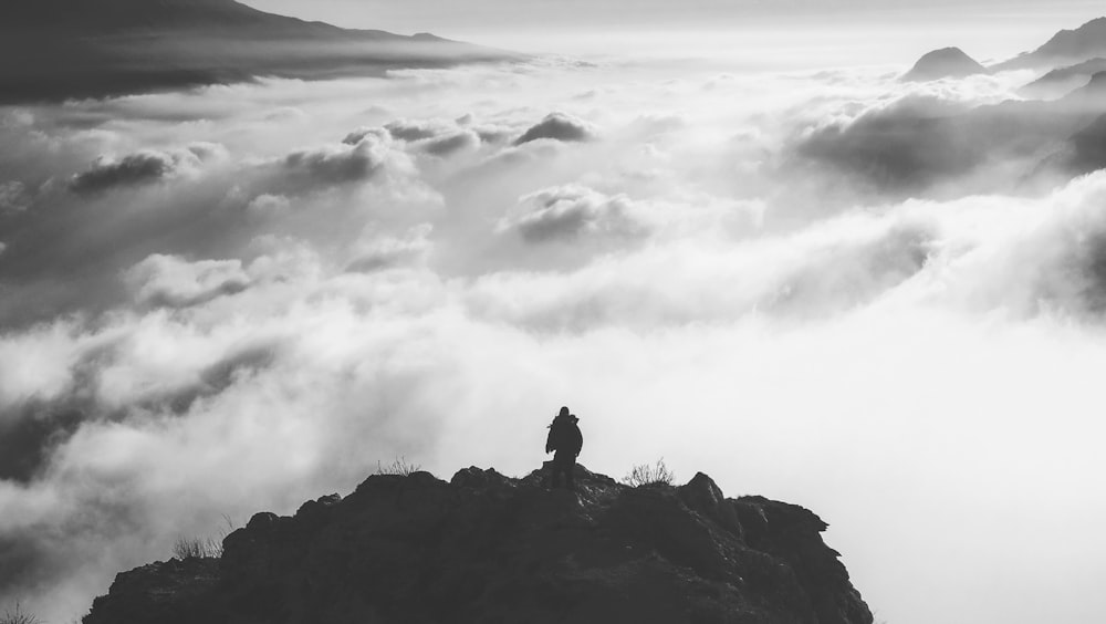 person standing at the edge of a mountain facing clouds during day