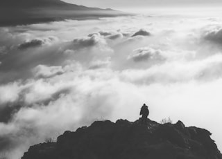 person standing at the edge of a mountain facing clouds during day